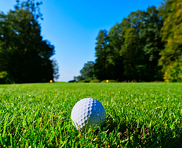Nahaufnahme eines weißen Golfballs im grünen Gras mit Bäumen im Hintergrund