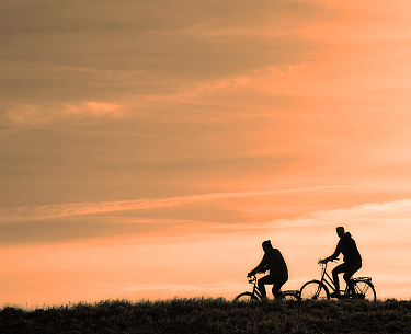 Zwei Radfahrer als Silhouetten vor einem orangefarbenen Sonnenuntergang
