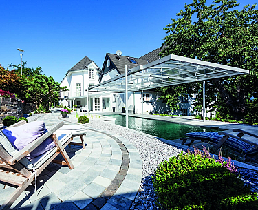 Moderne Terrasse mit Swimmingpool, Liegestühlen, Sonnenschirm und Gartenpflanzen