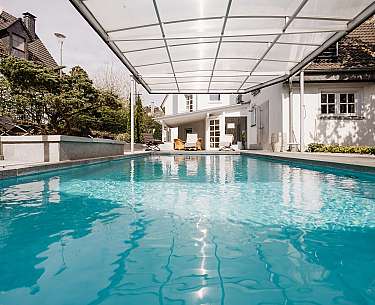Moderne Terrasse mit Swimmingpool, Liegestühlen, Sonnenschirm und Gartenpflanzen