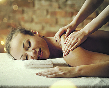 Frau liegt entspannt auf Massagebank, bekommt Schulter- und Nackenmassage